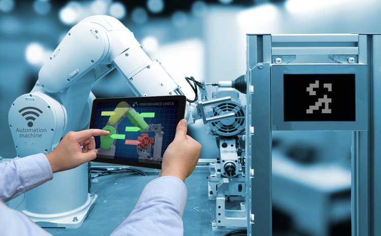 Person holding a tablet with performance check screen software, with an automated wireless robot arm in the background