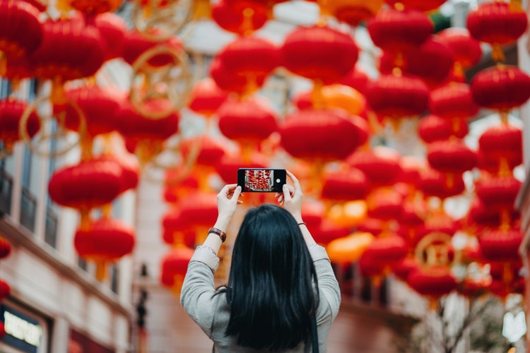 后景：一位女士在城市街上使用智能手机拍摄中国传统红灯笼的照片
