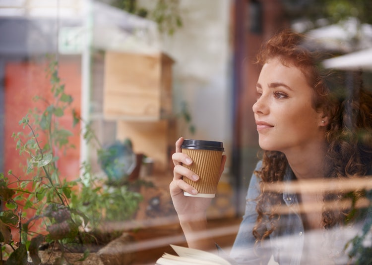 Woman contentedly looking out of an office window while holding a cup of coffee