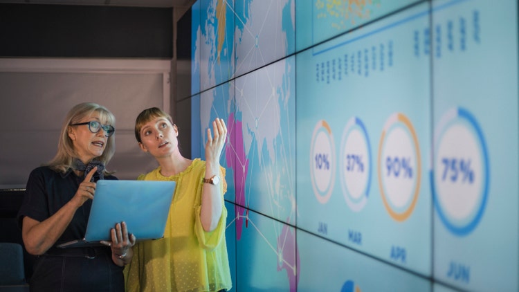 Two business people discuss data on digital screen