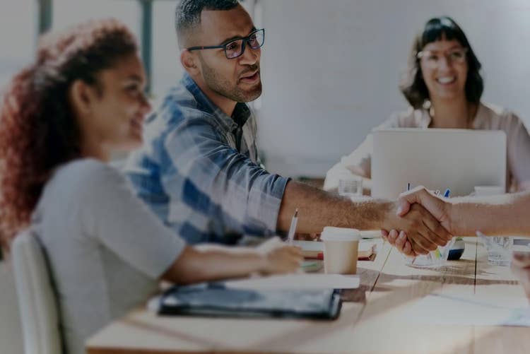 Employees engaged in a meeting, at which two men shake hands.