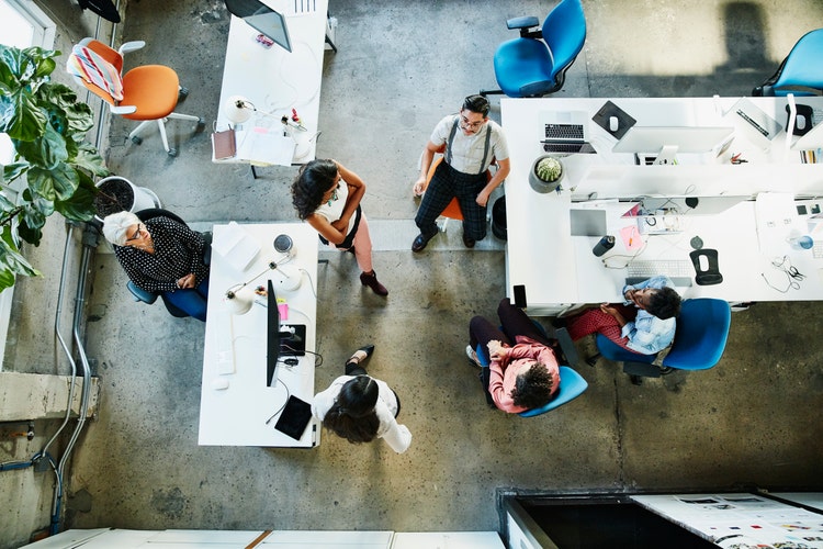 Bird’s-eye view of a diverse group of professionals gathered in a circle having a conversation at an open-concept workplace.