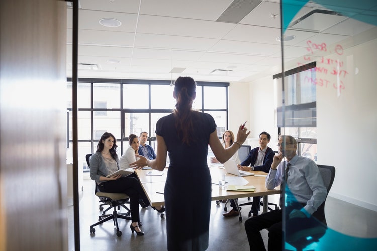 A businesswoman addresses serious-looking employees in a conference room