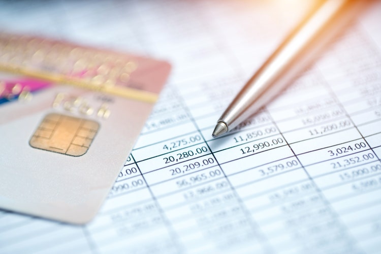 A printed spreadsheet showing a budget, with a credit card and pen arranged on top of it.