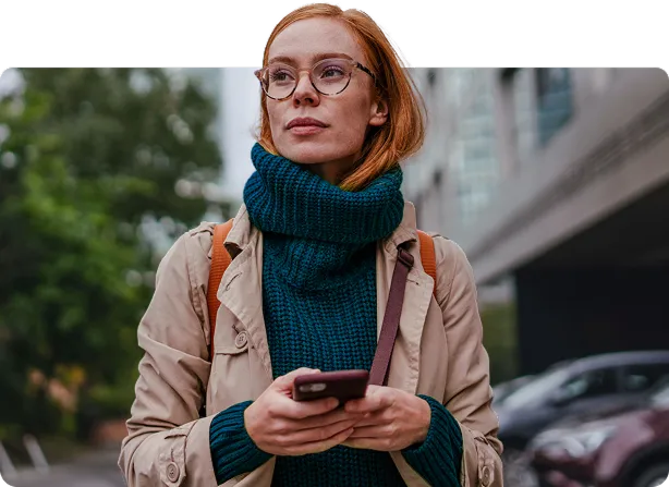 成年女性在秋日的城市街道上边走边使用智能手机——素材图片