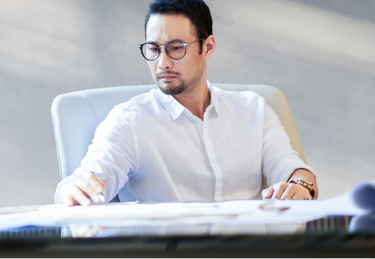 Asian bearded worker sitting, thinking and jotting notes indoors - stock photo