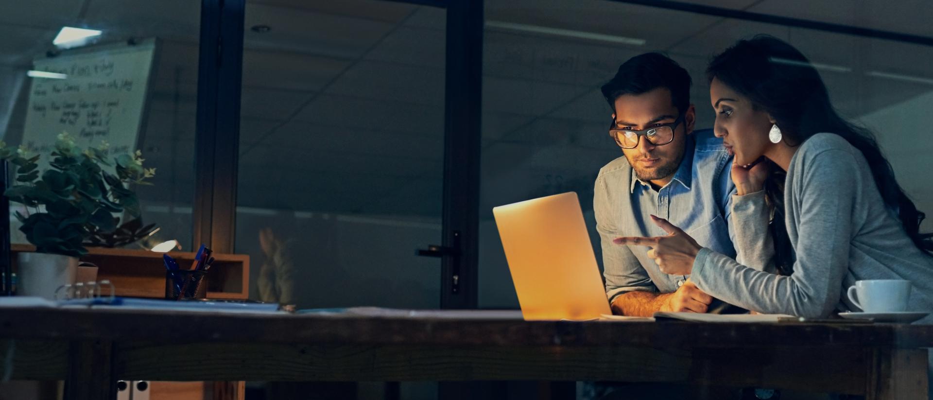 Two colleagues discussing and looking at laptop computer in an office