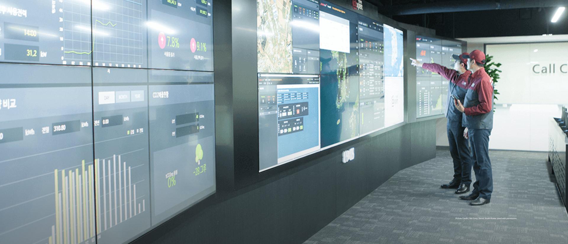 Two S and I Corp employees reviewing data on a digital wall