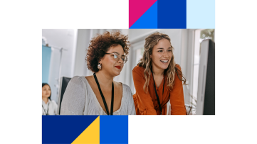 Two female colleagues smile as they work together on a computer in an office.