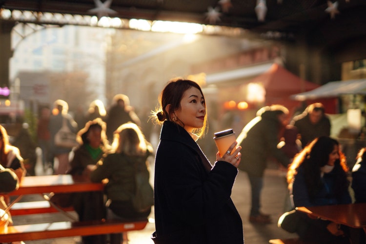 一位女士拿着杯咖啡，站在充满人的户外空间里