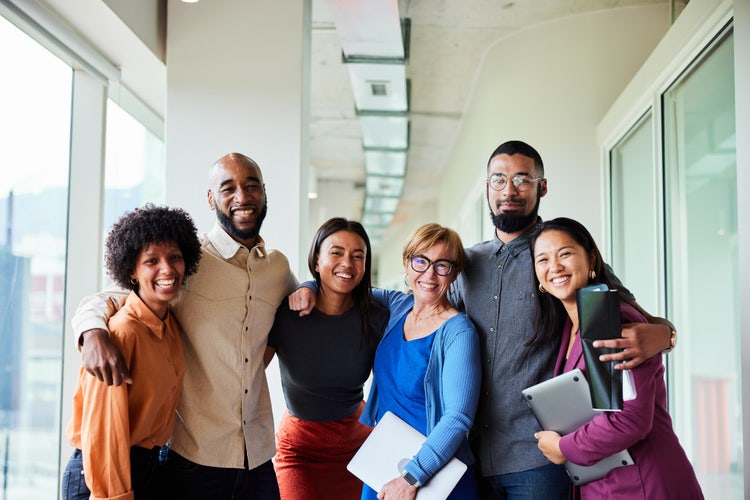 Business colleagues smiling and standing arm in arm, posing for a photo in an office hallway