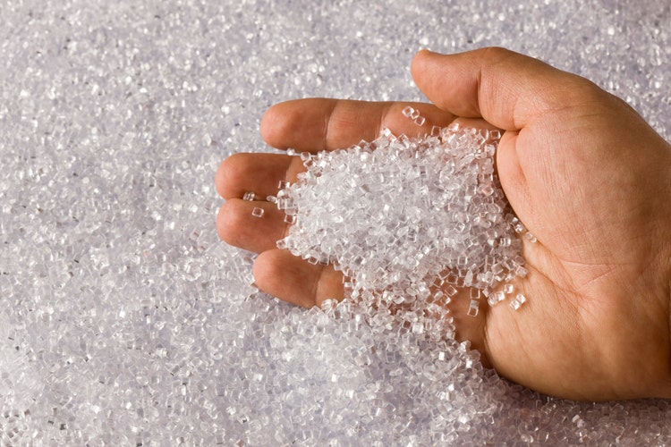 A hand scooping up small, round plastic resin pellets.