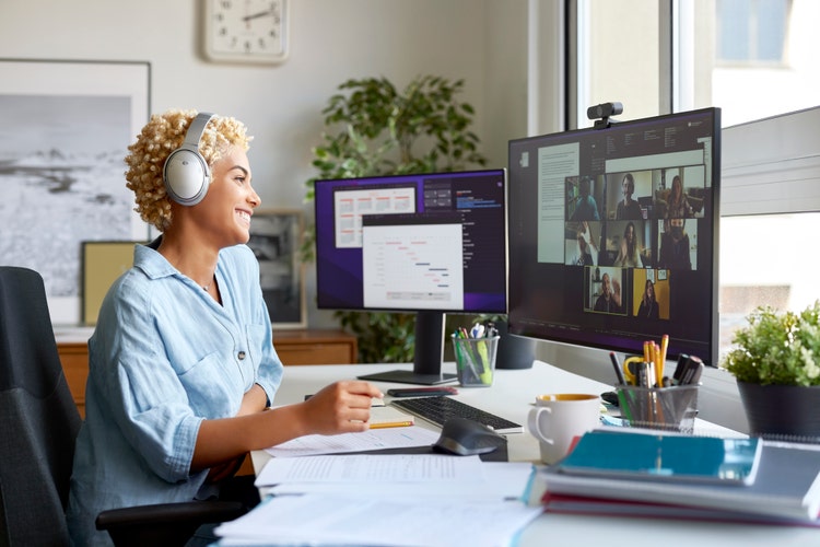 Businesswoman smiling and engaged in a video conference call, with colleagues visible on the screen, in a professional home office setting
